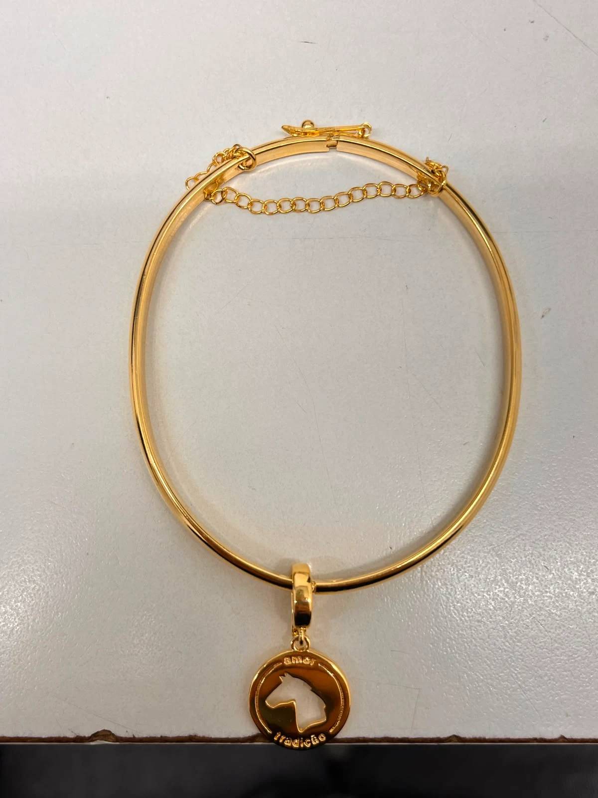 Bracelete dourado fotografado no celular, sobre a mesa de casa
